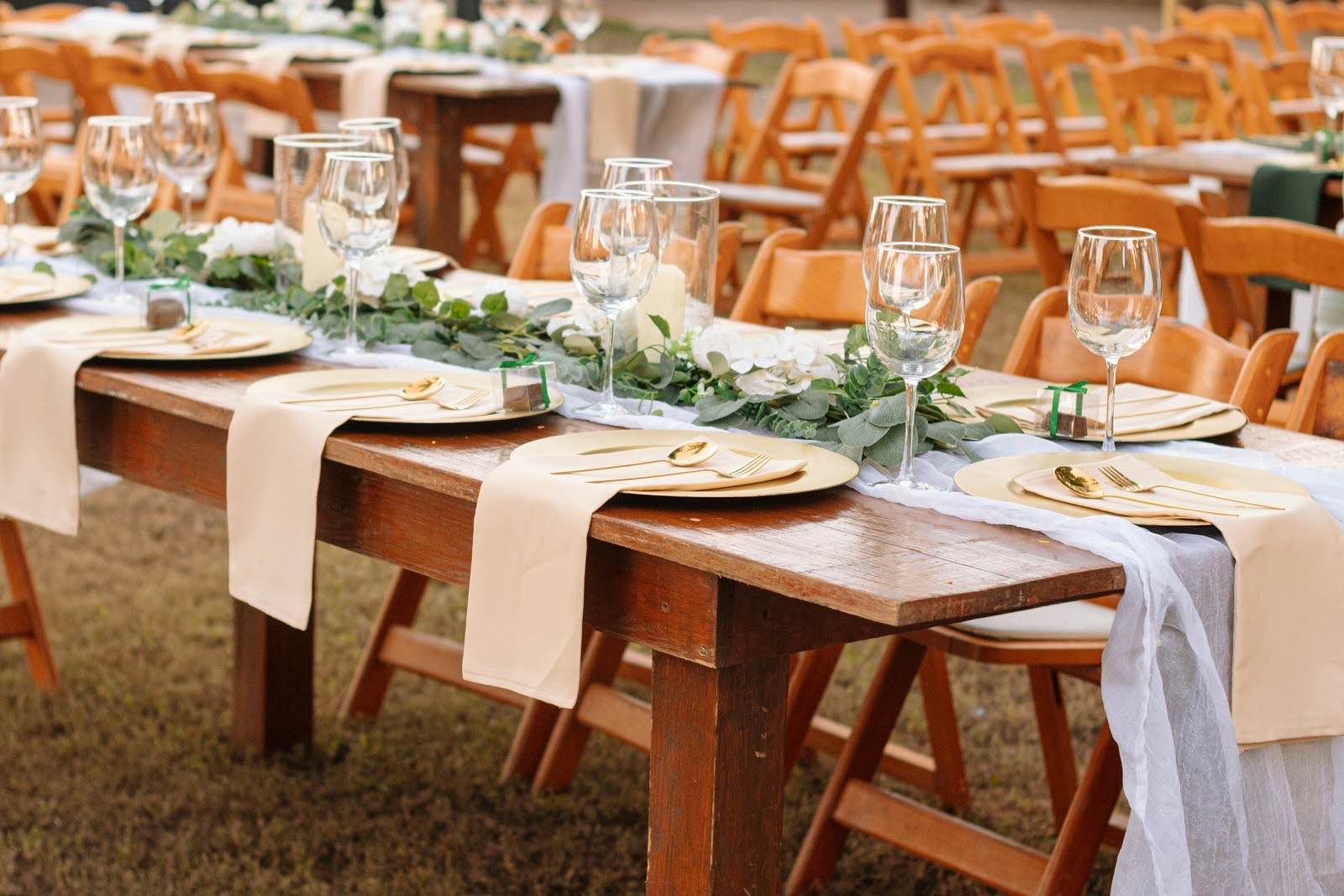 A long wooden reception table set with cream napkins, gold plates and a eucalyptus garland