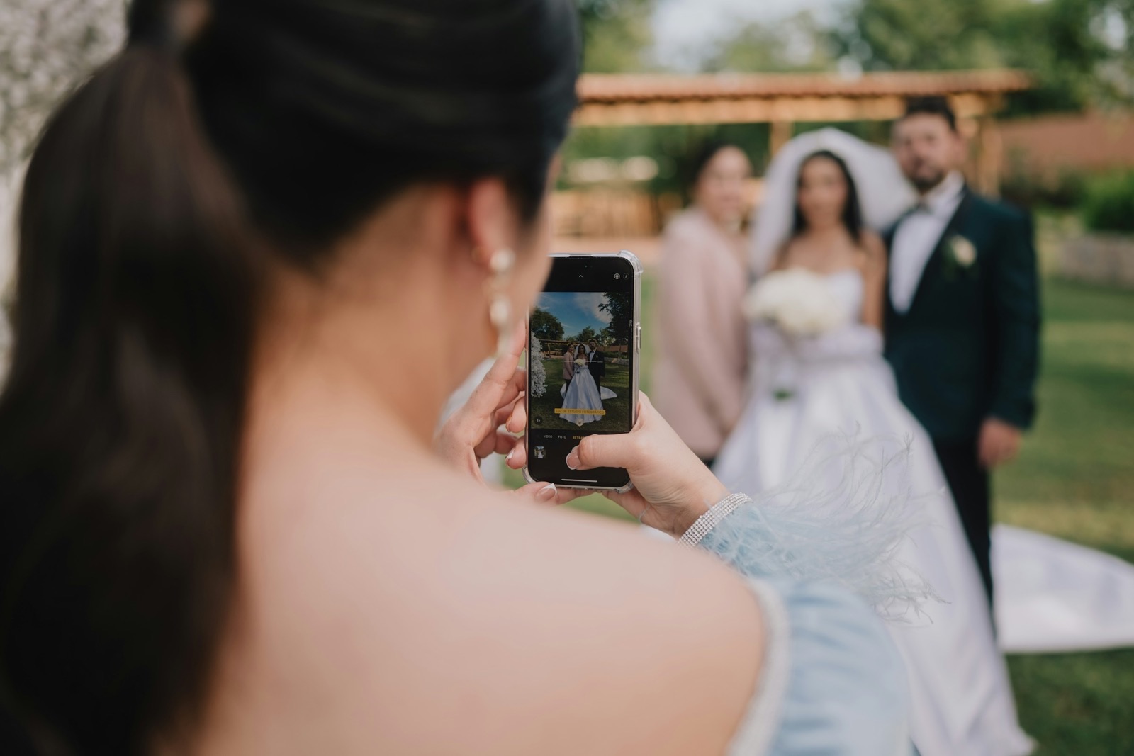 A wedding guest photographing the couple on her phone at an outdoor ceremony